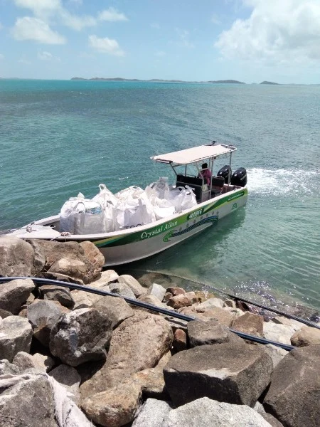 The Crystal Ailan boat carrying collection bags beside a rocky shoreline.