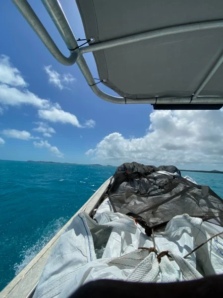 Collection bags and a dark covering aboard the boat, with open water and islands ahead.